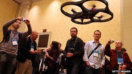 People looking at a drone controlled by an iPhone, shown in Nevada in 2010