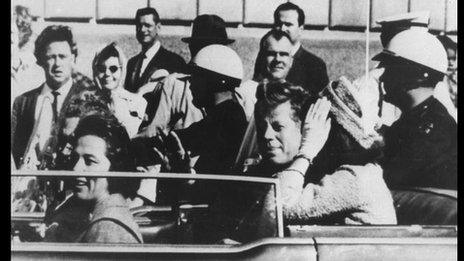 JFK, in Dallas on November 23rd 1963. JFK is seen in the back of the car as it passes close to the book depository, where Lee Harvey Oswald (the alleged assassin)