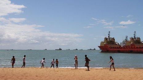 Children play on beach with oil ships in the background