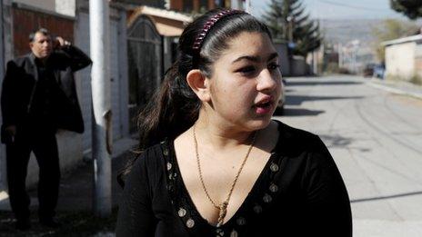 Leonarda Dibrani speaks to the media as her father Resat talks on his mobile phone outside their temporary home in Mitrovica