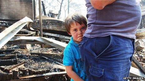 Lyndon Dunlop stands behind his father as they inspect the damage to his grandparents' home in Winmalee on 21 October 2013