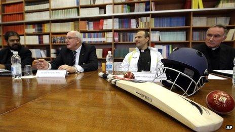 Vatican members discussing, with a cricket bat on the table