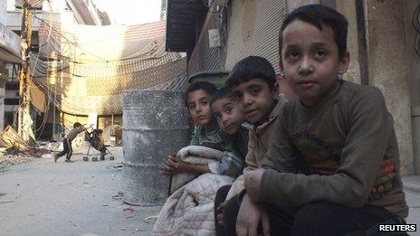 Children sit on a sidewalk of a street in the besieged area of Homs