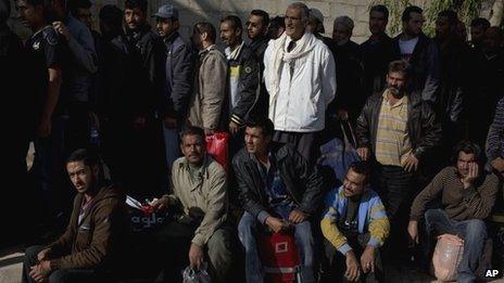 Men wait to be searched by the Syrian military