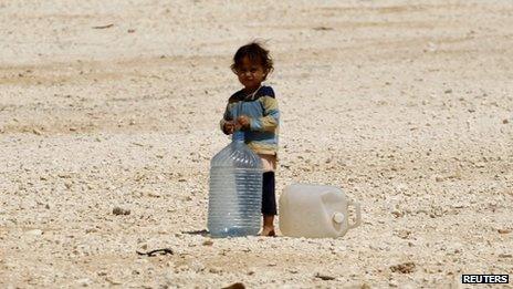 A young Syrian refugee stands beside water containers at the Zaatari refugee camp in the Jordanian city of Mafraq