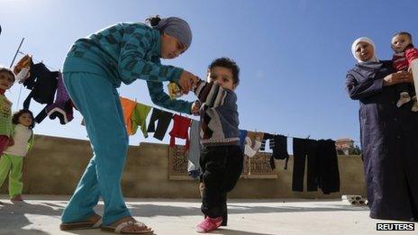 A Syrian refugee girl helps her brother, who the family suspects has polio, to walk