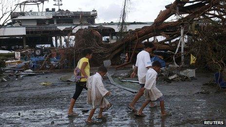 Survivors walk past a fallen tree outside an airport after super Typhoon Haiyan battered Tacloban city