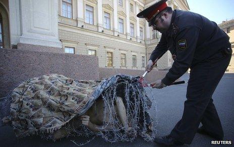 Artist Pyotr Pavlensky lies on the ground, wrapped in barbed wire roll, during a protest action in St Petersburg on 3 May 2013