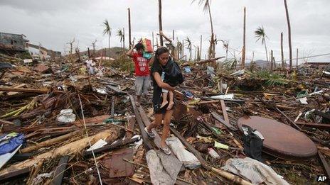 A woman carries her baby across an area damaged by Typhoon Haiyan at Tacloban city, Leyte province, central Philippines on 12 November 2013