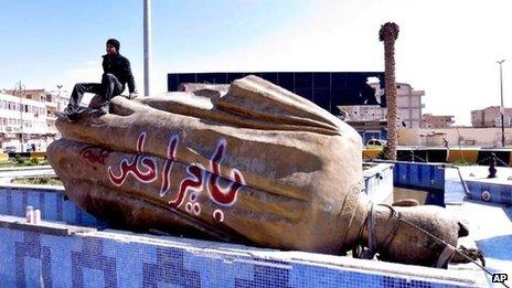 A man sits on a statue of President Hafez al-Assad in Raqqa