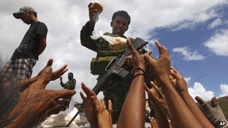 A soldier hands out food to a crowd. People's hands are outstretched towards him