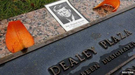 A photo of Kennedy with flowers on a plaque at Dealey Plaza in Dallas, Texas