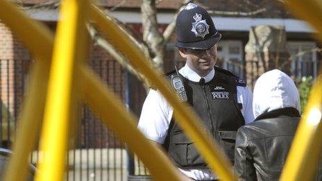 A male police officer speaks to a person wearing a hooded jumper with the hood pulled up