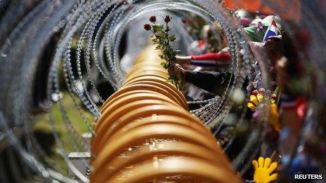 Anti-government protesters give roses, through razor wire, to the security personnel guarding the Defence Ministry as protesters gather outside it in Bangkok on 28 November 2013