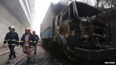 Fire fighters walk past a vehicle set on fire by protesting workers