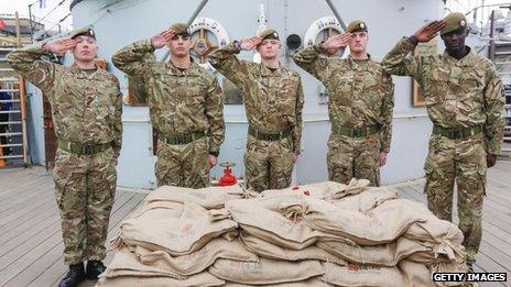 Five soldiers salute as they stand guard over bags of soil collected from Belgium's WW1 battlefields on board a navy ship