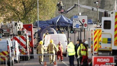 A road packed with emergency services personnel, with a tarpaulin on the roof of a pub in the background