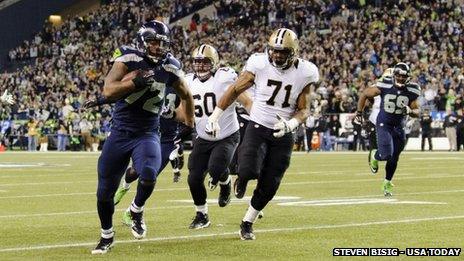 Seattle Seahawks defensive end Michael Bennett (left) runs the ball for a touchdown during a game at CenturyLink Field in Seattle, Washington, on 2 December 2013