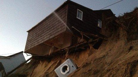 A beach chalet hanging over a beach after the ground beneath it collapsed