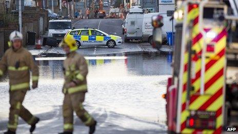 Firefighters and a police car separated by a flooded road