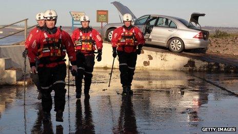 Humberside fire and rescue officers check a flood-damaged car blown on to the banks of the Humber Estuary flood defence wall