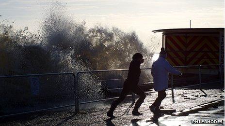 Two people run away from a wave hitting Lowestoft