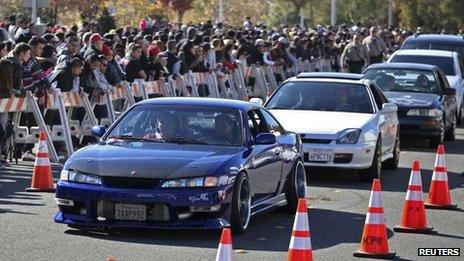 Vehicles are driven past a crowd attending an unofficial memorial event for Fast & Furious star Paul Walker