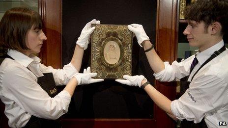 Two people wearing white gloves hold a portrait of Jane Austen