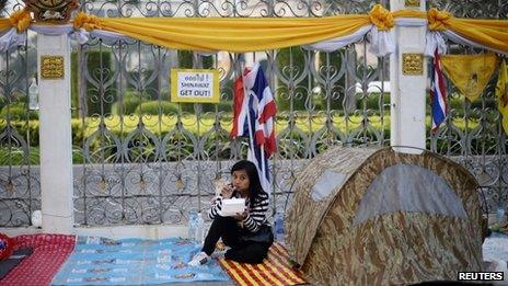 An anti-government protester eats breakfast as she wakes up outside Government House in Bangkok on 10 December 2013