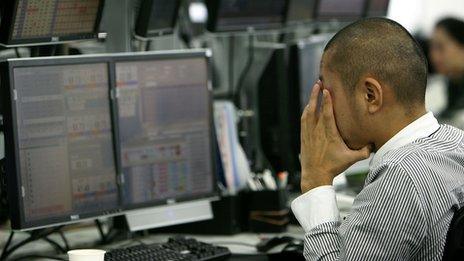 A currency trader in Tokyo rubs his eyes as he works in front of multiple computer screens