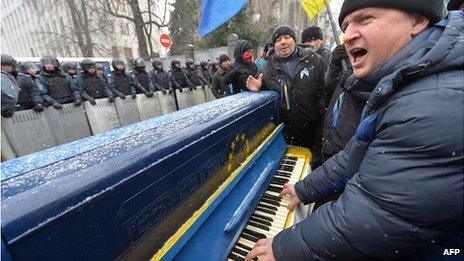 A man plays piano and sings songs in front of riot police as protesters picket Viktor Yanukovych's presidential office in Kiev