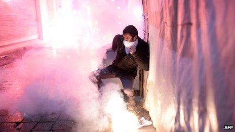 A Turkish protestor protects himself as fireworks explode on the Istiklal Avenue on December 27, 2013, during clashes between the Turkish police and protestors