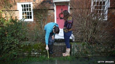 A man uses a stick to test the depth of water outside a house