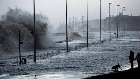 Waves rolling over a sea wall and flooding the pathway behind it