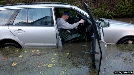 A man sits in a car with the door open - flood water is up to the driver's seat