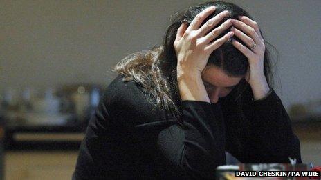 A woman leans on a desk with her head in her hands