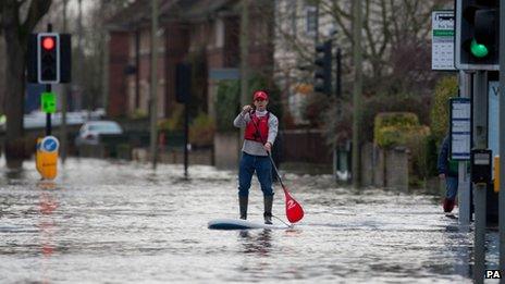 A man paddles a surfboard along a flooded road