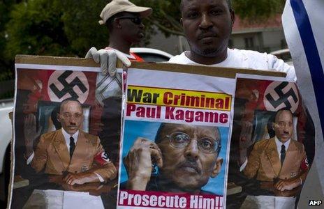 A member of the Rwanda National Congress opposition party holds a picture and sketches of Rwandan President Paul Kagame portrayed as a Nazi leader and reading "war criminal" during a demonstration outside the Rwandan embassy in Pretoria on January 9, 2014.