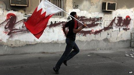 A Bahraini anti-government protester runs with a national flag during clashes with riot police firing tear gas in Sanabis, Bahrain, 18 October 2013