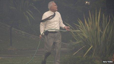 A local resident uses a garden hose to protect his home from a fast-moving California wildfire 16 January 2014