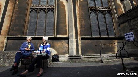 Two women wearing party rosettes sitting outside a church