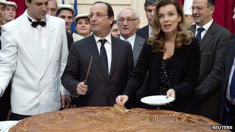 French President Francois Hollande (L) and Valerie Trierweiler (R) cut slices of a giant traditional Epiphany cake during a ceremony at the Elysee Palace in Paris on 7 January 2014