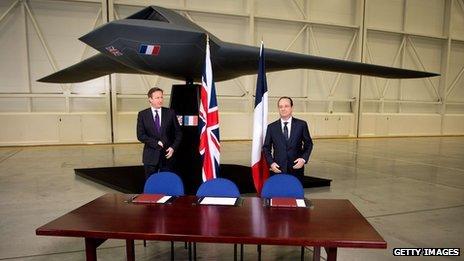 British Prime Minister David Cameron (L) and French President Francois Hollande stand beneath a model of an unmanned aircraft before holding a press conference during a one-day summit at RAF Brize Norton