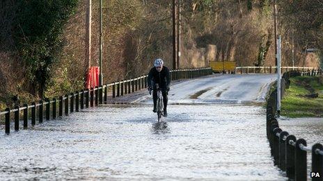 A cyclist rides drives through a flooded road next to the River Thames in Chertsey, Surrey