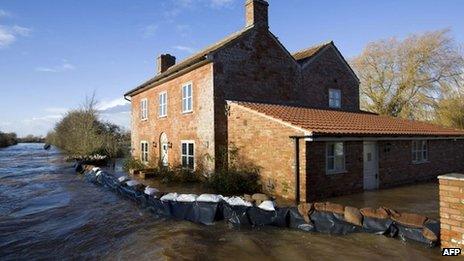 A house surrounded by sandbags - with flood water on both sides of the barrier