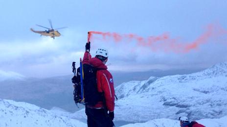 A mountain rescue team member holds a red flare as the RAF helicopter approaches