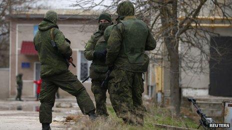 Armed men, believed to be Russian soldiers, stand next to a heavy machine gun as they stand guard at an Ukrainian military base in Yevpatoria