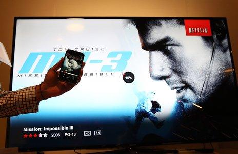 Someone is holding a phone and appearing to control a TV with Netflix on it