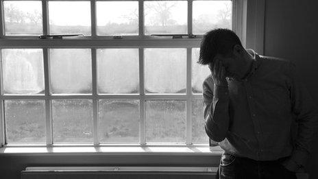 A man stands by a window with his head in his hands