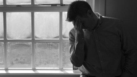 A man stands by a window with his head in his hands